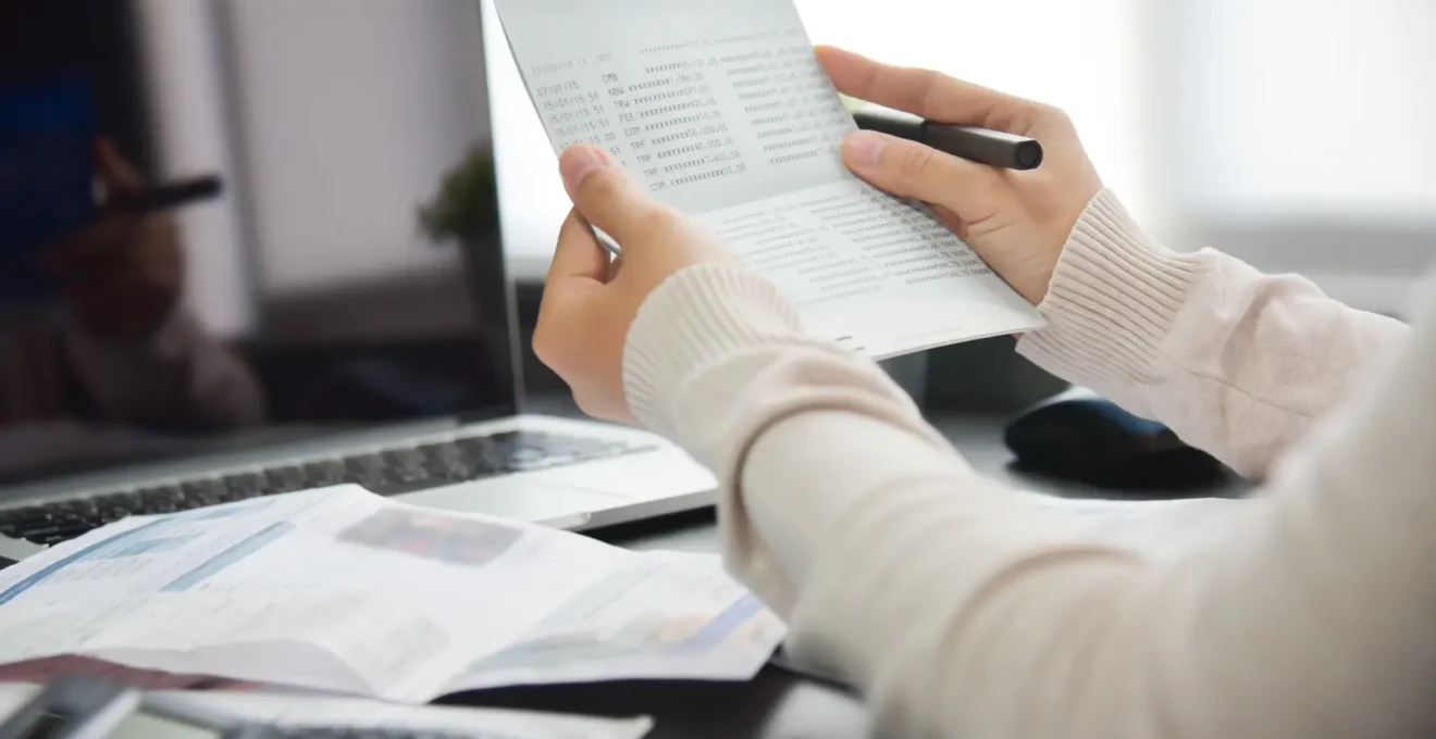 Des mains comparent un livret d'épargne et un relevé sur un bureau.